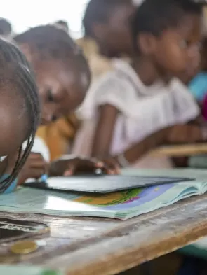 Young girl sitting at a desk and writing on a miniature chalkboard with a piece of chalk